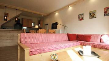 Un salón acogedor con un sofá rojo estampado, suelo de madera y una mesa de comedor con sillas.