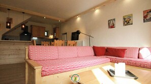 Ein gemütlicher Wohnbereich mit einem rot gemusterten Sofa, Holzboden und einem Esstisch mit Stühlen.