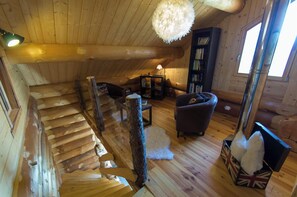 A log cabin interior with a wooden staircase, a fireplace, a sofa, and a bookshelf. - THE CAPUCHIN HUT (CHANTEPERIER)
