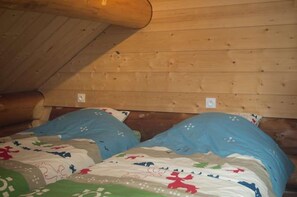 A wooden cabin room with two beds, each with a blue pillow and a patterned bedspread. - THE CAPUCHIN HUT (CHANTEPERIER)