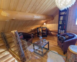 Ein gemütliches Blockhaus-Interieur mit einem Glastisch, Ledersofas, einem Bücherregal und einer Pendelleuchte.