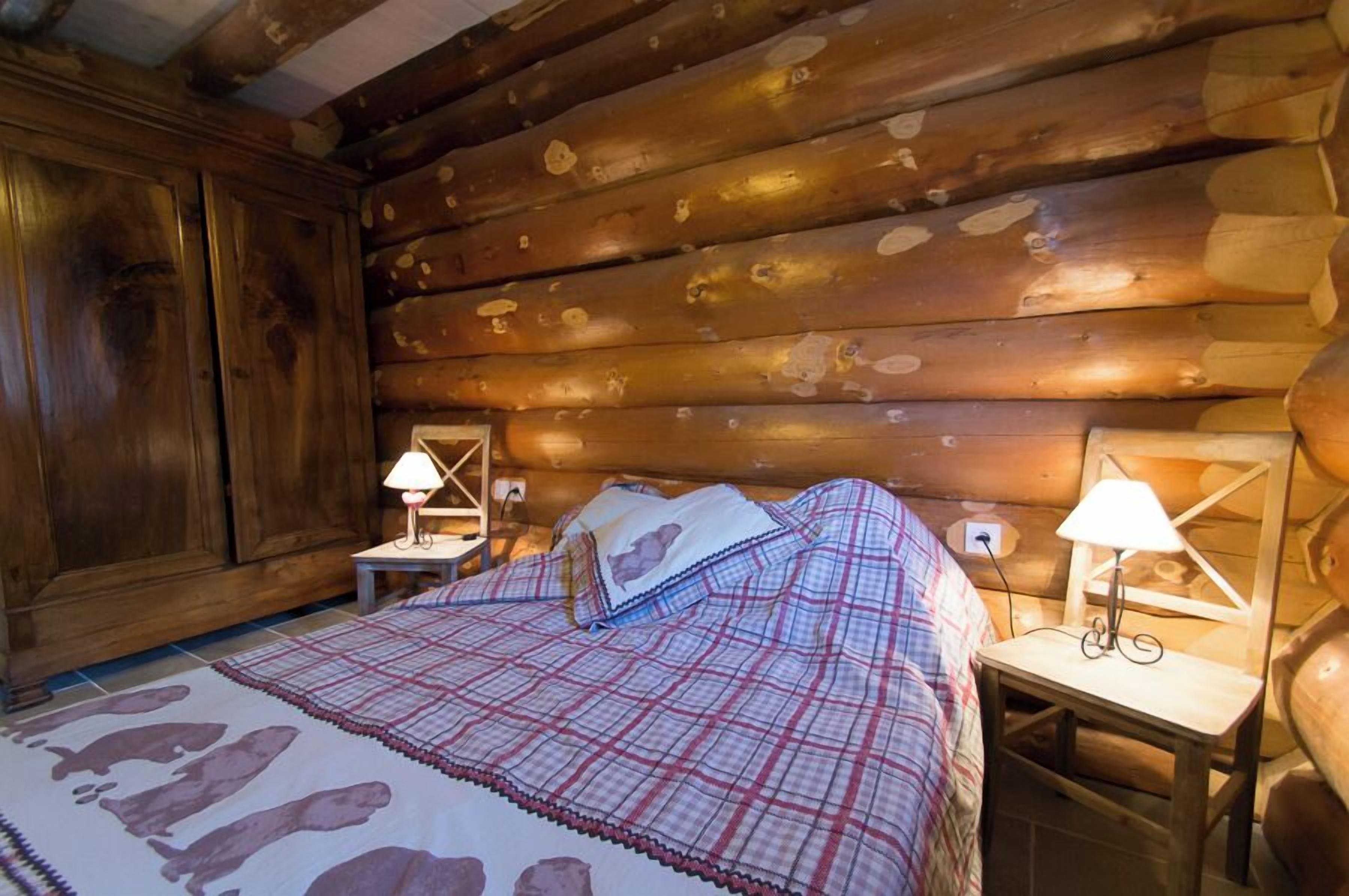A log cabin bedroom with a bed, two bedside tables, and a wooden wardrobe.