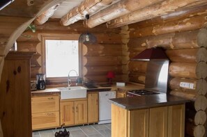 Eine Küchenzeile in einer Blockhütte mit Holzschränken, einer Spüle, einem Herd und einem Fenster.