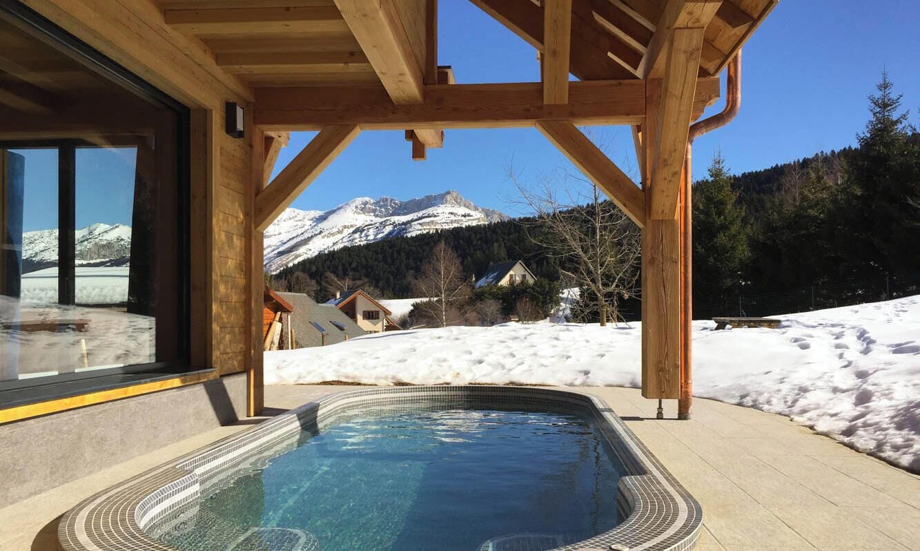 A wooden deck with a hot tub overlooking a snowy landscape and mountains.