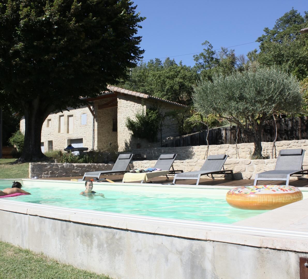 Une piscine avec des chaises longues et, en arrière-plan, un bâtiment en pierre.