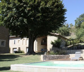 Ein Steinhaus mit Pool, einem großen Baum und einer Holzterrasse.
