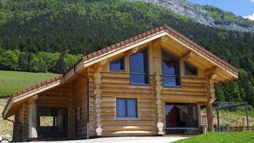 Une cabane en rondins avec un toit en pente, de grandes fenêtres et une véranda couverte.
