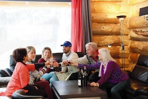 Un groupe de personnes est assis sur un canapé à l’intérieur d’une cabane en rondins, une table se trouvant entre elles.