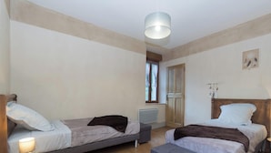 A bedroom with two single beds, a wooden wardrobe, a radiator, and a ceiling light fixture.
