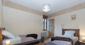 A bedroom with two single beds, a wooden wardrobe, a radiator, and a ceiling light fixture.