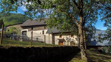 A stone building with a sloped roof, surrounded by a stone wall and a fenced area.