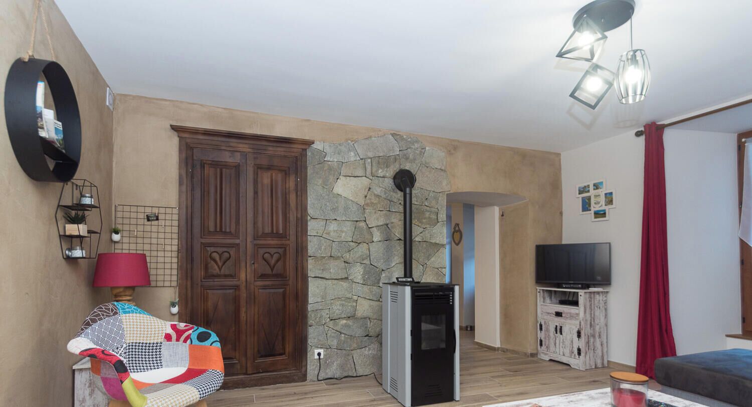 A living room with a stone wall, a wooden door, a television, and a red curtain.