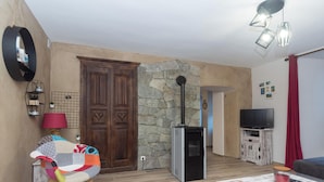 A living room with a stone wall, a wooden door, a television, and a red curtain.