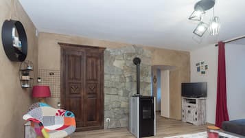 A living room with a stone wall, a wooden door, a television, and a red curtain.