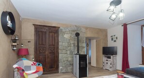 A living room with a stone wall, a wooden door, a television, and a red curtain.
