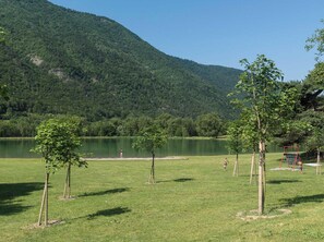 A grassy field with a lake and trees, a goalpost, and a person in the distance.