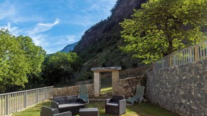 A patio area with outdoor furniture, a stone wall, and a view of a mountainous landscape.
