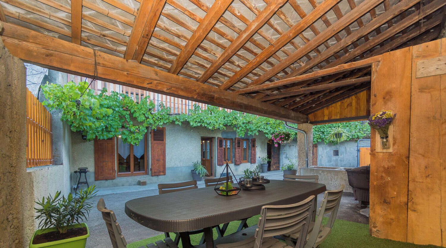 Eine Terrasse im Freien mit einer Holz-Pergola, einem runden Tisch und Stühlen.