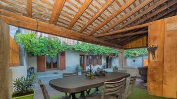 Patio esterno con una pergola in legno, un tavolo rotondo e sedie.