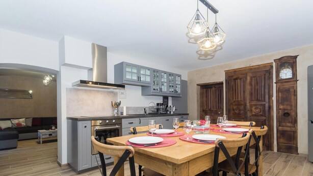 A modern kitchen with grey cabinets, a wooden dining table set for four, and a built-in oven.