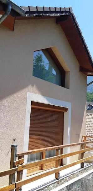 A building with a sloped roof, a large garage door, and a wooden balcony railing. - LE CLOS FLEURI URIAGE (URIAGE LES BAINS)