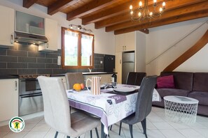 A modern kitchen with a dining area, featuring a stove, oven, and refrigerator. - LE CLOS FLEURI URIAGE (URIAGE LES BAINS)