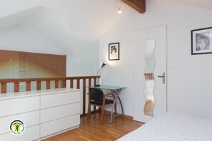 A bedroom with a bed, a desk, and a chair. There is a window with blinds, a door with a mirror, and a light fixture. - LE CLOS FLEURI URIAGE (URIAGE LES BAINS)