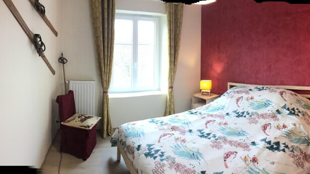 A bedroom with a bed, two bedside tables with lamps, a chair, a radiator, and a window with curtains.