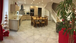 A modern kitchen with a dining area, a staircase, and a living room with red furniture and a glass coffee table.