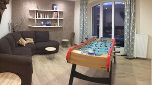 A living room with a sofa, a small round table, a bookshelf, and a foosball table.