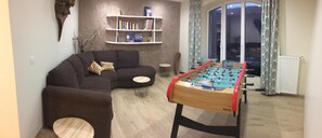 A living room with a sofa, a small round table, a bookshelf, and a foosball table.