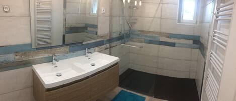 A bathroom with a double sink vanity, a shower, and a small window.
