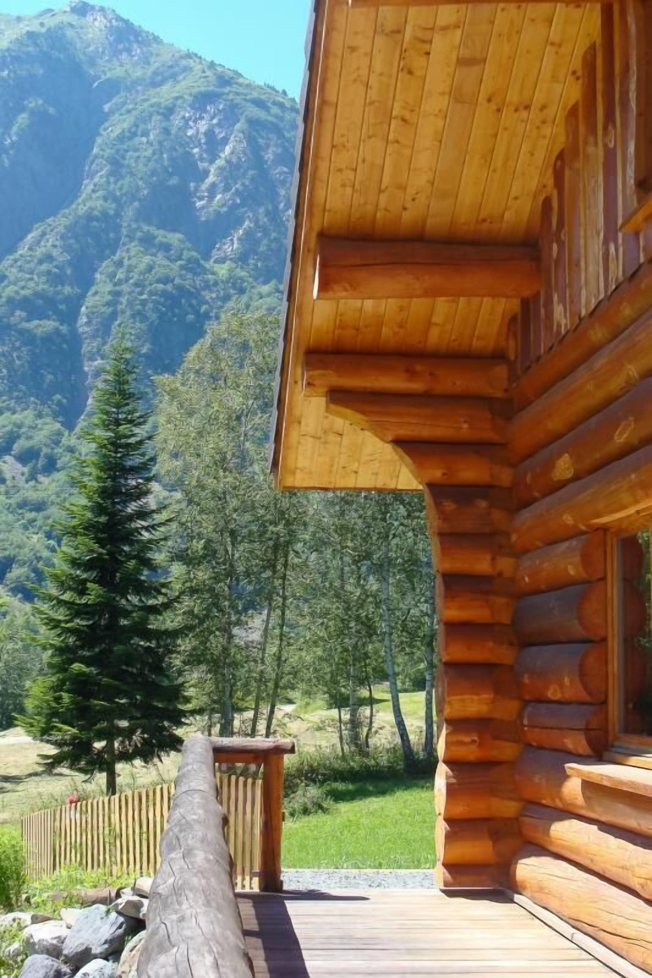 A wooden cabin with a deck, surrounded by a mountainous landscape.