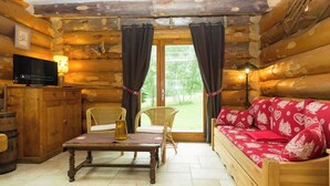 A log cabin interior with a wooden sofa, wicker chairs, a television, and a table. - CHANTELOUVE / LE BECAN (CHANTEPERIER)