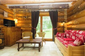 Ein rustikales Blockhaus-Interieur mit einer Holzbank, Korbsesseln, einem Fernseher und einem Tisch.