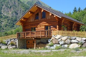 Eine Blockhütte mit einem Balkon, umgeben von einer Steinmauer und einem Holzzaun.