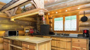 A log cabin kitchen with a central island, wooden cabinets, a microwave, a stove, and a window with a calendar. - CHANTELOUVE / LE BECAN (CHANTEPERIER)