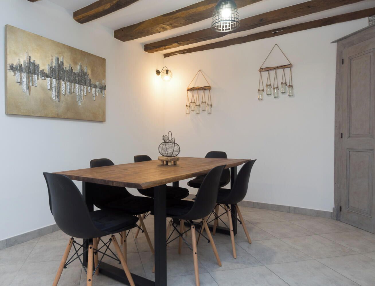Ein Essbereich mit einem Holztisch und schwarzen Stühlen, einem Stadtbildgemälde an der Wand und einer Pendelleuchte.