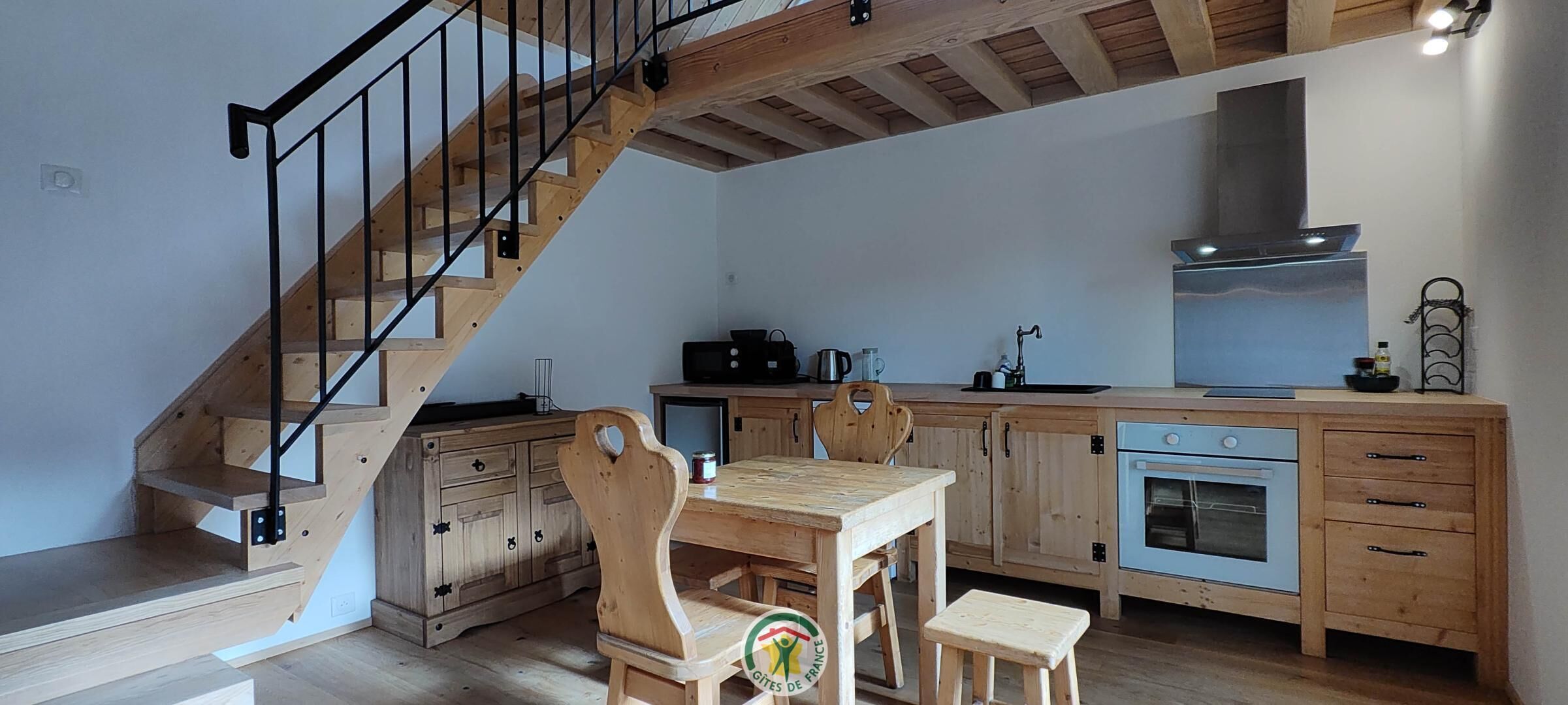 Eine Küche mit Holzausstattung, einem Esstisch, Stühlen, einem Backofen und einer Treppe mit Holzwertlauf.