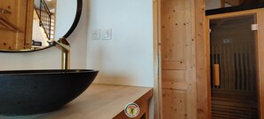Un intérieur en bois avec un lavabo noir posé sur un comptoir, un miroir et une porte dotée d’un panneau en bois.