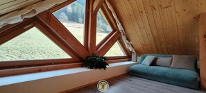 Une pièce chaleureuse avec un plafond en pente, de grandes fenêtres, un canapé et une plante.