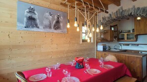A dining area with a red tablecloth, wooden walls, and a kitchen in the background. - La Darse - VILLARD RECULAS (VILLARD RECULAS)