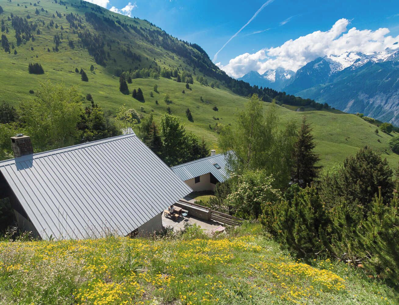 Een huis met schuin dak, omgeven door een weelderig groen landschap en bergen op de achtergrond.