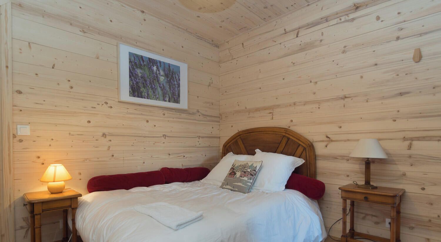 A wooden-paneled room with a bed, two bedside tables, a wall-mounted lamp, and a framed picture.