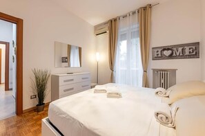 Una camera d'albergo con un letto, un comodino, una lampada, una pianta in vaso e un cartello con la scritta 'HOME'.