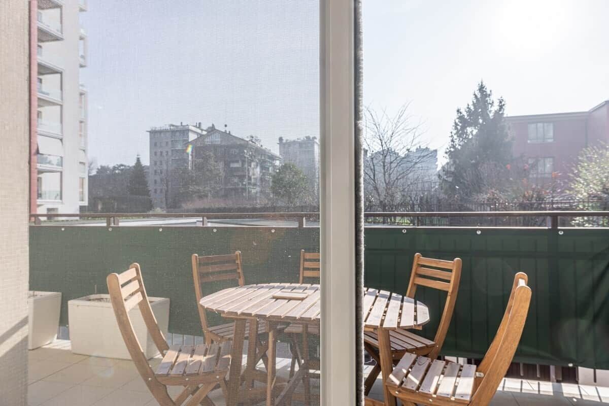 Un balcone con tavolo e sedie, vista su edifici e un recinto verde.