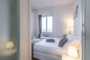 Een hotelkamer met een bed, een raam met gordijnen, een radiator en een lamp.