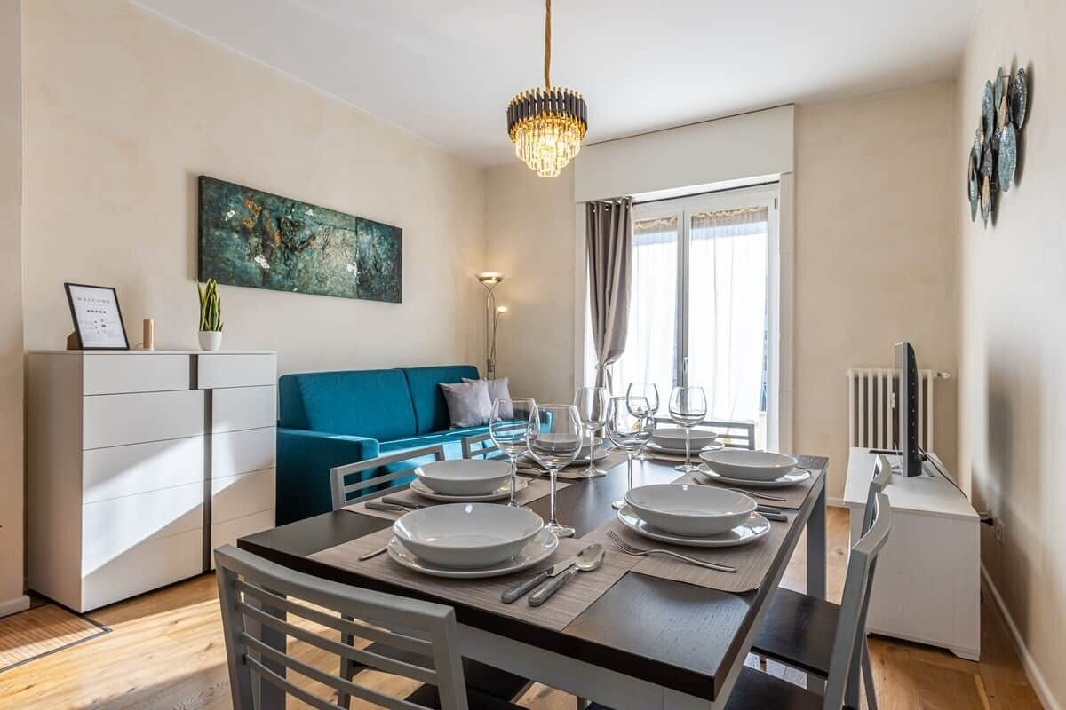 A dining area with a table set for four, a blue sofa, a white cabinet, and a painting on the wall.