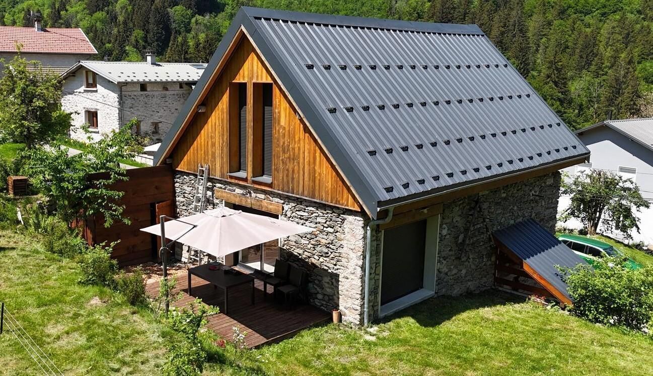 A modern house with a sloped metal roof, stone walls, and a wooden deck with outdoor furniture.
