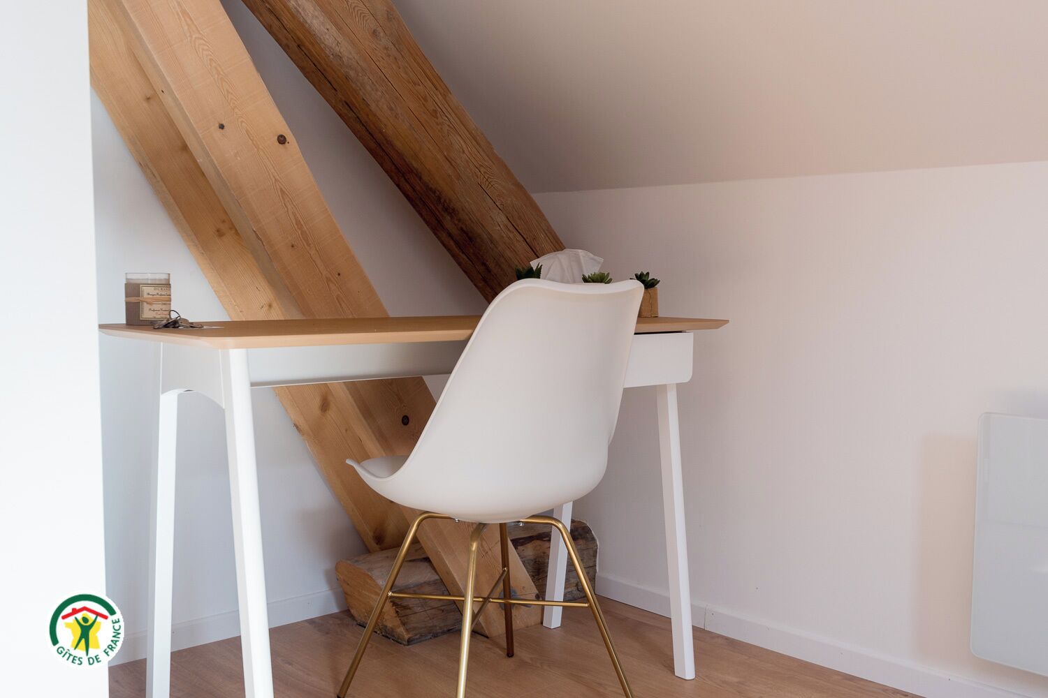Ein modernes Zimmer mit weißem Schreibtisch und Stuhl, Holzbalken und einer kleinen Pflanze auf dem Schreibtisch.